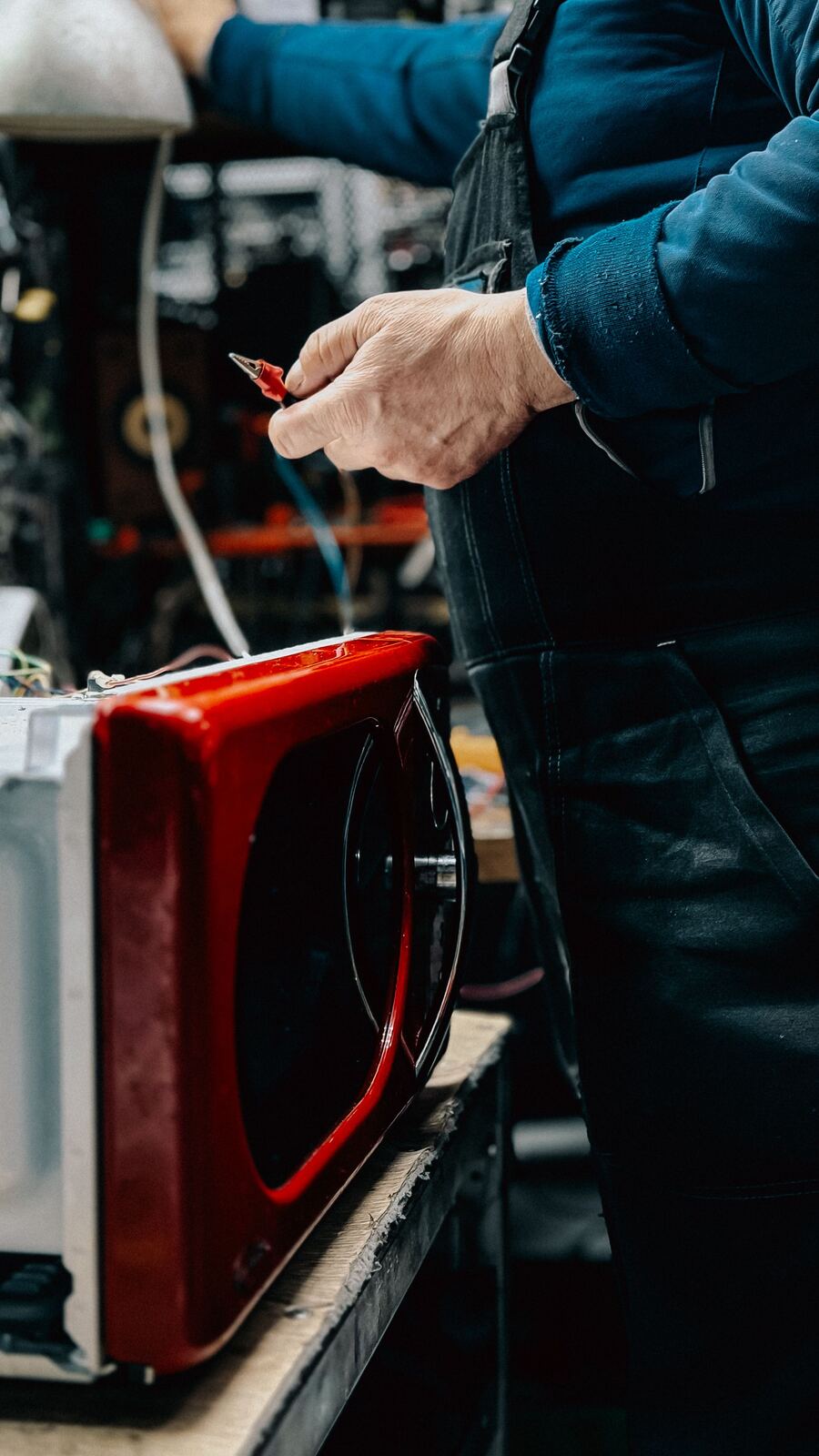 Technician holding a test lead next to a red microwave oven