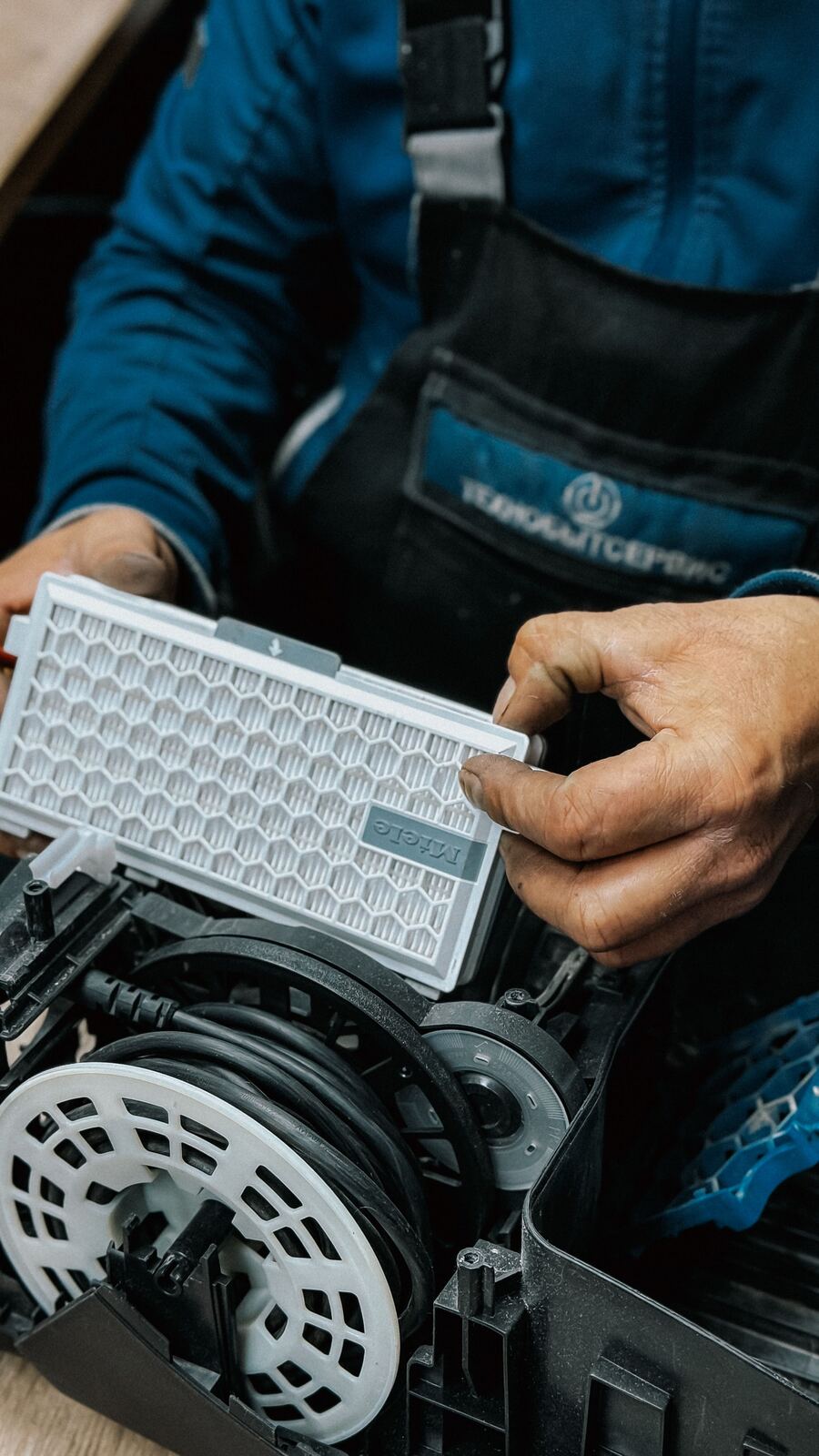 Hands holding a replacement HEPA filter above an opened vacuum cleaner